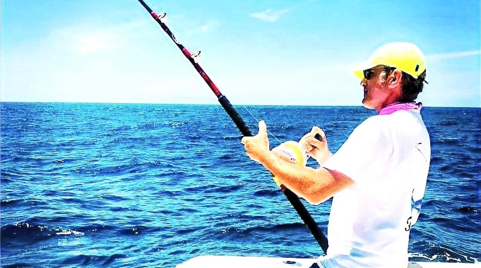 Pescador con la caña doblada peleando un pez desde la proa de un barco en la Bahía de Banderas, Puerto Vallarta